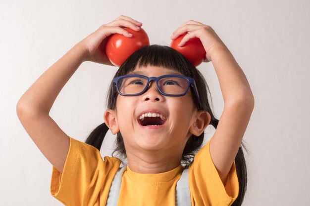 Foto chiuda sul bambino che tiene i pomodori sulla sua testa. ragazza carina soddisfatta della verdura.