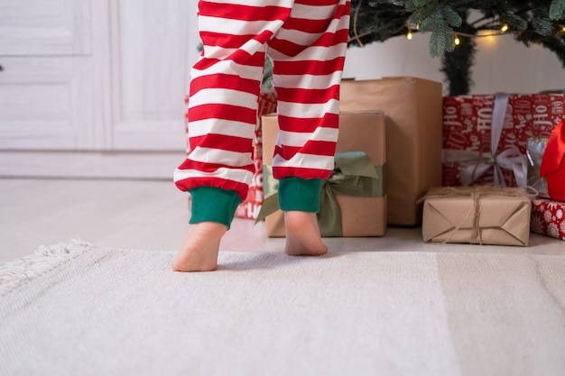 close up kid legs in Christmas pajamas near gift boxes and Christmas tree