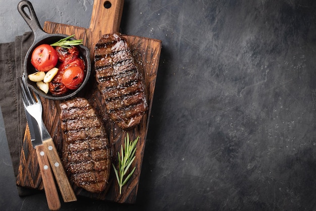 Close-up klaar om steak te eten Top Blade rundvlees rassen van zwarte Angus met grill tomaten knoflook en op een houten bord Het afgewerkte gerecht voor het diner op een donkere stenen achtergrond Top view met kopieerruimte