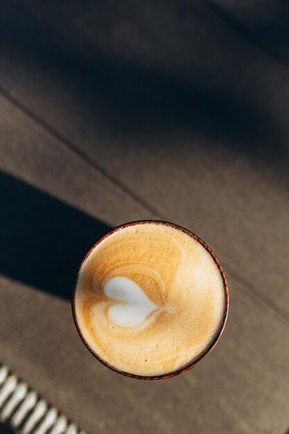 Close-up kopje warme cappuccino koffie met hartvormige latte art op donkerbruine oude houten tafel in café eten en drinken concept De zon schijnt op de beker