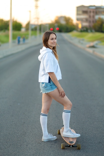 Close up of lady leg in white sneakers resting after extreme funny ride her wooden longboard skateboard. Modern urban hipster girl have fun. Good sunny summer day for skateboarding and have fun