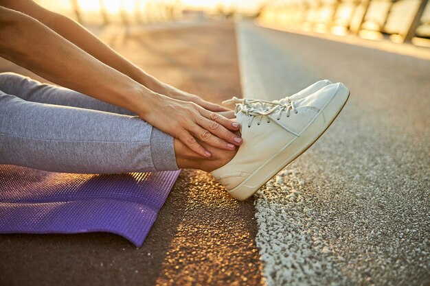 close up of lady in white sport shoes touching her legs while resting on asphalt road