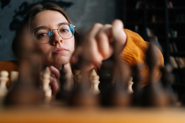 Foto close-up lage hoekmening van jonge vrouw in elegante bril die schaken bewegen met ridder stuk zittend in de vloer kijkend naar camera