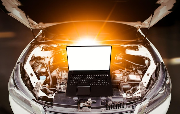 Close up of laptop computer with blank screen on car engine compartment background Car maintenance service concept