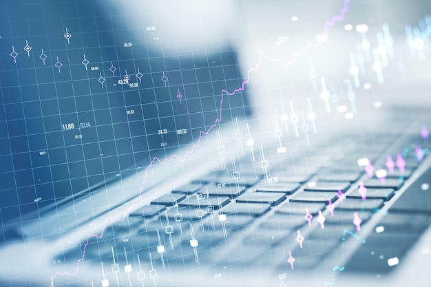 Close up of laptop on desk with glowing forex chart and grid on blurry background Stock financial growth and trade concept Double exposure