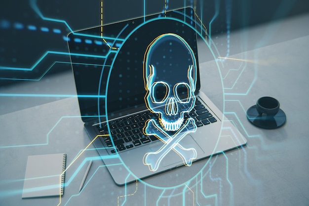 Close up of laptop on desk with notepad coffee cup and digital skull hologram on blurry background Hacking malware and crime concept Double exposure