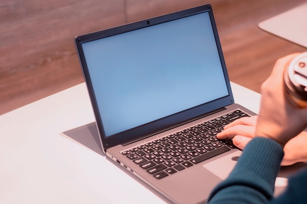 Close-up laptop mockup with white screen. A male freelancer works in a cafe.