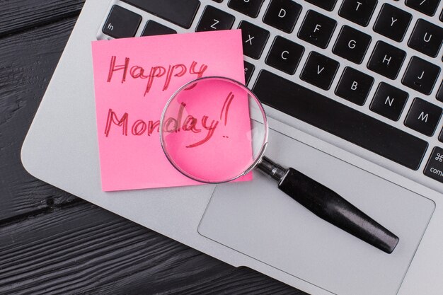 Photo close up laptop with glass magnifier and happy monday wish. dark wooden background.