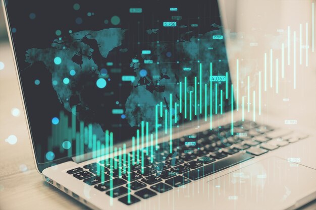 Photo close up of laptop with growing blue forex chart and map hologram on blurry background banking invest and financial growth concept double exposure