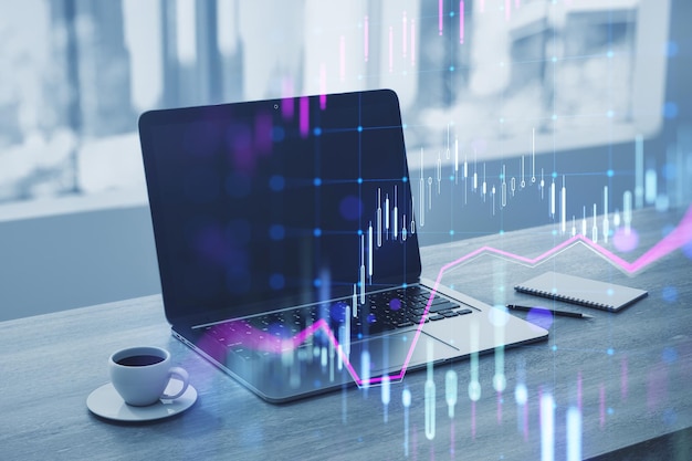 close up of laptop at workplace with coffee cup supplies and glowing candlestick forex chart on blurry wallpaper technology trade and financial data concept double exposure