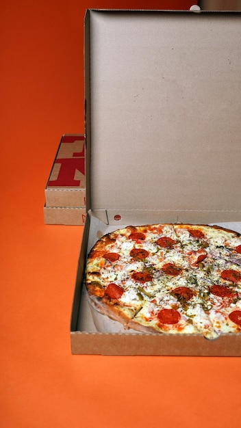 Close up of large pizza in box on orange background Appetizing pizza with different ingredients