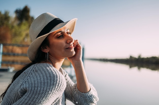 Close up of Latin woman with hat relaxing on the edge of a dock next to a lake