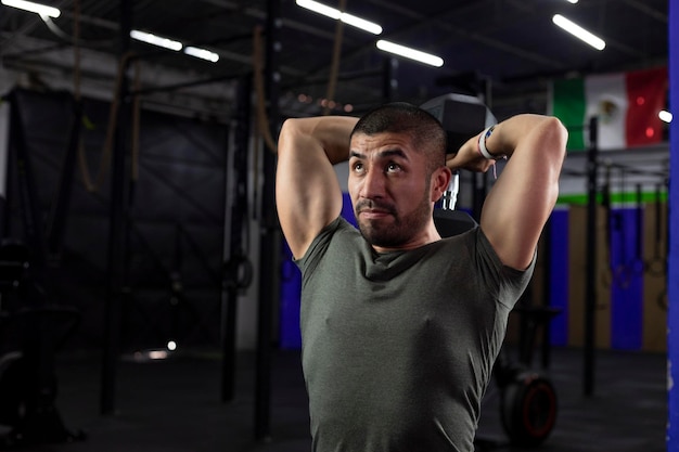 Close up of a latino athlete doing triceps exercise in a gym with a dumbbell