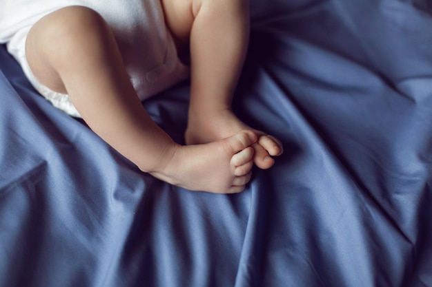 침대에 누워 있는 색 바디슈트를 입은 금발의 다리 아기