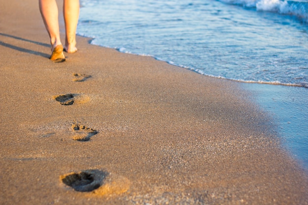 Primo piano di gambe, impronte sulla sabbia e onde del mare