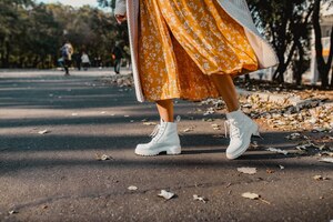 Крупным планом ноги в стильной белой обуви обуви молодой женщины в желтом платье с принтом в солнечный осенний день, весело