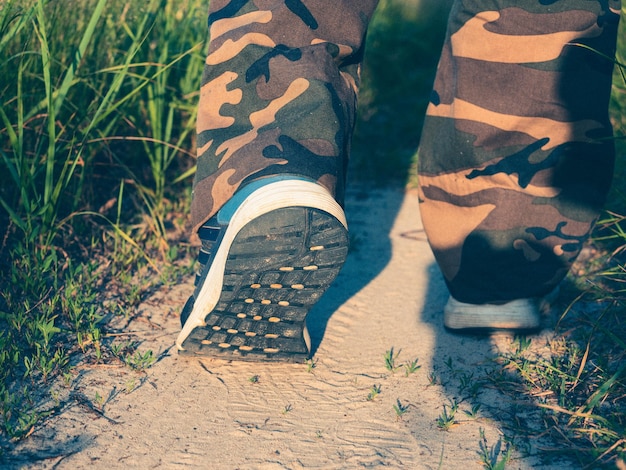 숲 속 길을 따라 걷는 운동화를 입은 남자의 다리 클로즈업. 하이킹, 걷기, 그리고 스포티한 라이프스타일의 개념. 배면도