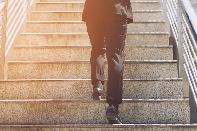 Close up legs shoes of young business man one person walking\
stepping going up the stairs in modern city go up success grow up\
with filter tones retro vintage warm effect stairway