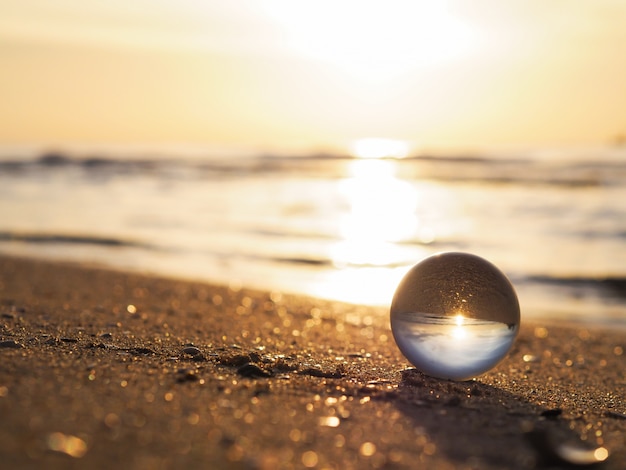 Close up lens ball with golden sunrise reflection at summer beach. 