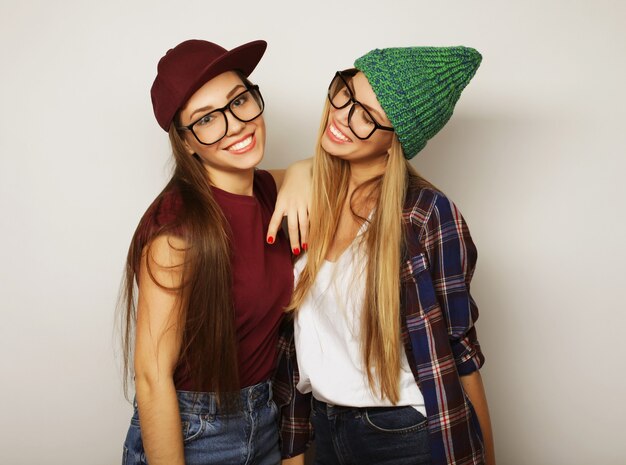 Close-up lifestyle portret van twee mooie tiener vriendinnen glimlachen en plezier hebben, hipster kleding, bril en hoeden dragen, positieve stemming.