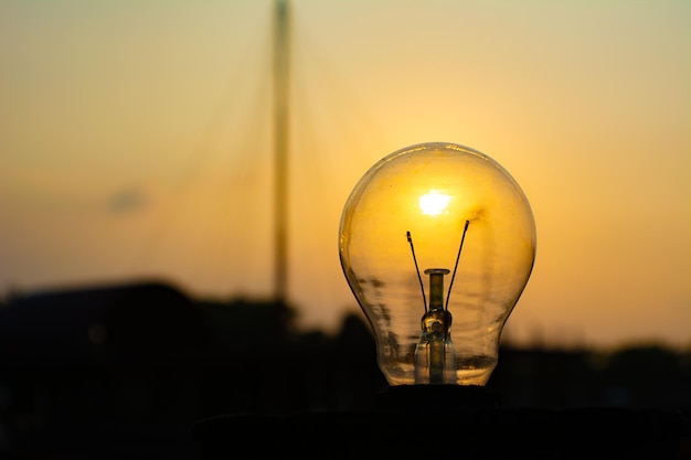 Close-up of light bulb against silhouette landscape during sunset