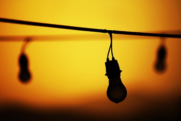 Photo close-up of light bulbs hanging against sky during sunset