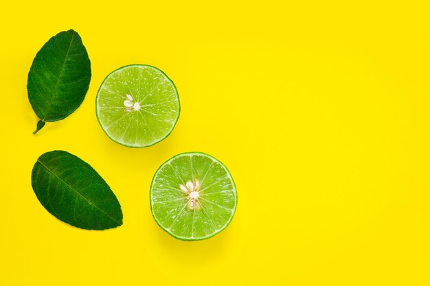 Close-up of lime slices with leaves on yellow background