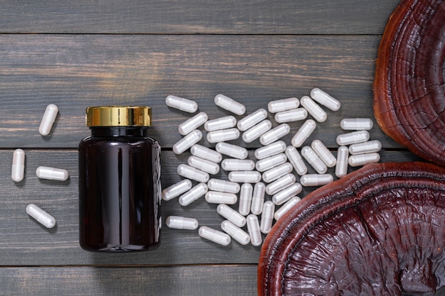 Close up of Ling zhi mushroom, Ganoderma lucidum mushroom and capsule with bottle mockup on wood table