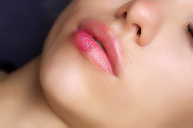 Close-up of the lips of a young model who has a tattoo on her lips made up to the middle