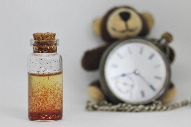 Photo close-up of liquid in bottle by stuffed toy and pocket watch against white background