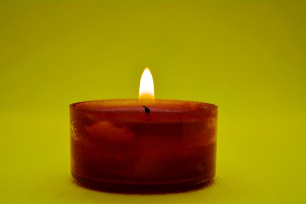 Close-up of lit candle against yellow background