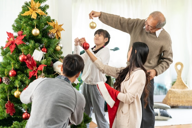 Close up on little Asian girl decorating a Christmas tree with ornaments