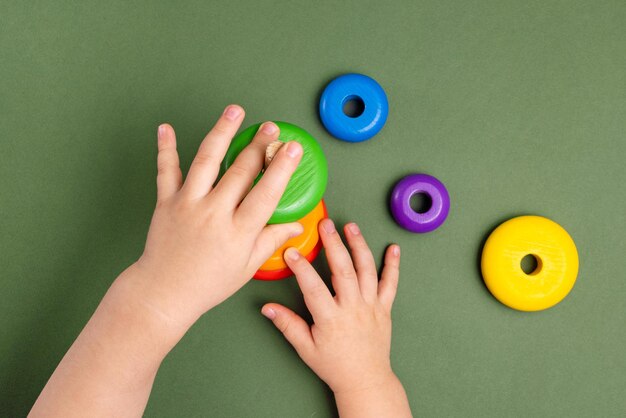 Close up of little baby wearing pajamas playing with wooden toy pyramid on green background natural