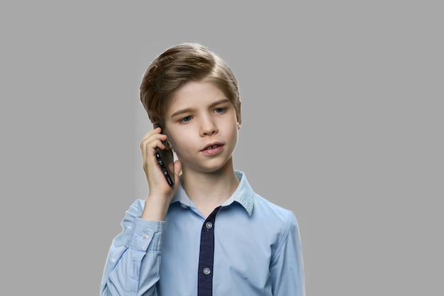 Close up little boy talking on mobile phone. Handsome child using cell phone on gray background. Children, modern technology, communication.