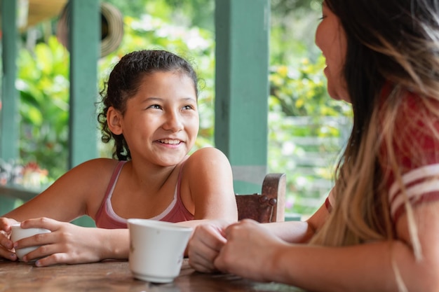 Foto up vicino di piccola bruna ragazza latina sorridendo mentre guarda sua madre bere caffè o tè