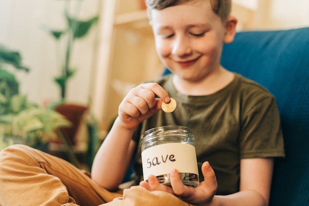 Close up of little child kid boy hands grabbing and putting stack coins in to glass jar with save