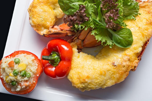 Close up lobster bake with cheese sliced in half serviced with fire rice in tomato.