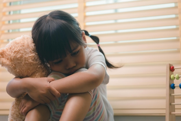 Close up lonely little girl hugging toy sitting at home alone upset unhappy child waiting for parents thinking about problems bad relationship in family psychological trauma