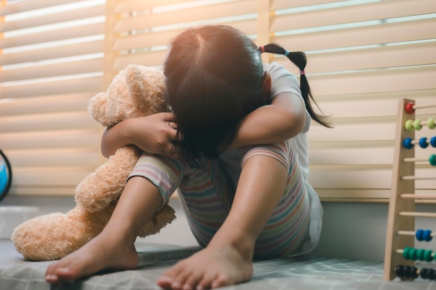 Primo piano bambina solitaria che abbraccia il giocattolo seduto a casa da solo sconvolto bambino infelice in attesa che i genitori pensino ai problemi cattiva relazione nel trauma psicologico familiare