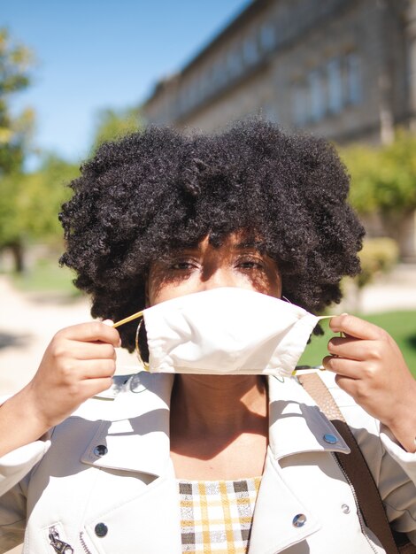 コロナウイルスを防ぐために白い保護マスクで若い黒人女性のクローズアップ、屋外、孤立