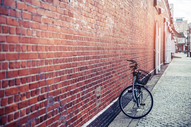 屋外の赤レンガの壁の近くに一人で立って素敵な黒い自転車を閉じます。