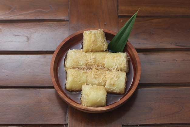 a close up of lupis with grated coconut and brown sugar sauce served in a wooden bowl Indonesian traditional food photo concept