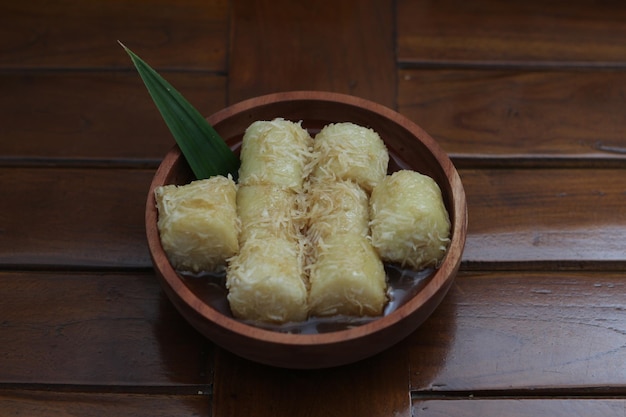 a close up of lupis with grated coconut and brown sugar sauce served in a wooden bowl Indonesian traditional food photo concept