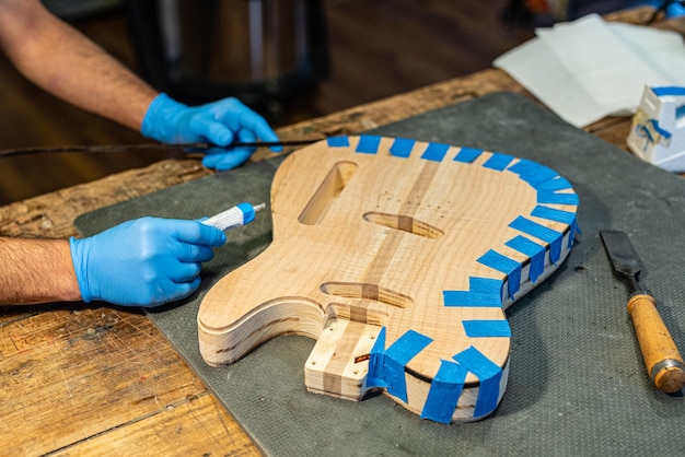 Close-up of a luthier's hands at work on the body of a guitar, hands of a craftsman with protective gloves, music business and construction of musical instruments