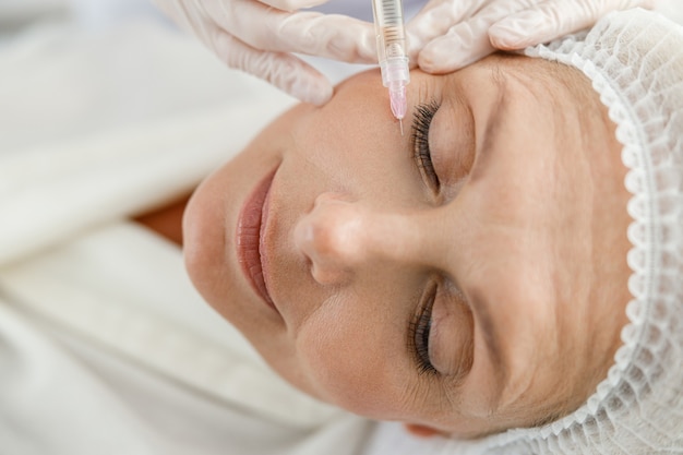 Close-up maakt mesotherapie-injecties voor een oudere vrouw.