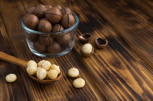 Foto primo piano su noci di macadamia in un cucchiaio di legno e fiocco di vetro sul tavolo