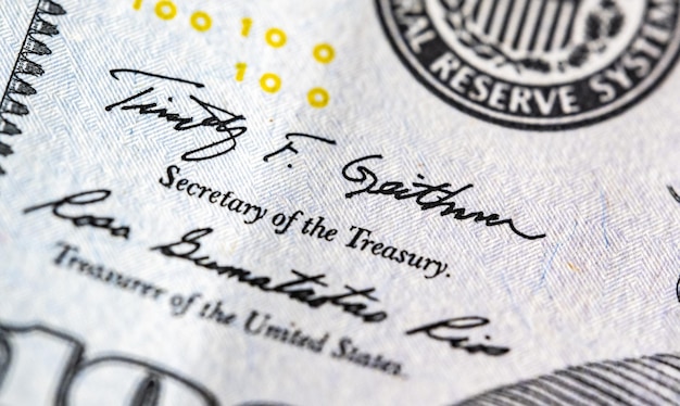 미국 재무부 표지가 있는 100달러 지폐 조각의 매크로 보기를 닫습니다.