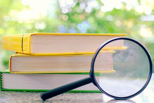 Foto prossimo piano di una lente d'ingrandimento con una pila di libri sul tavolo