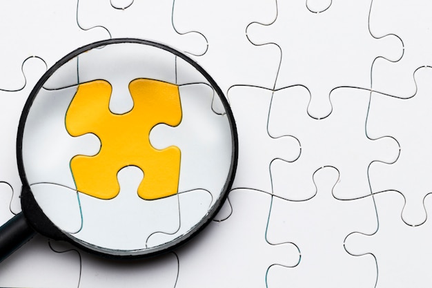 Close-up of magnifying glass over yellow puzzle piece connected with white puzzle