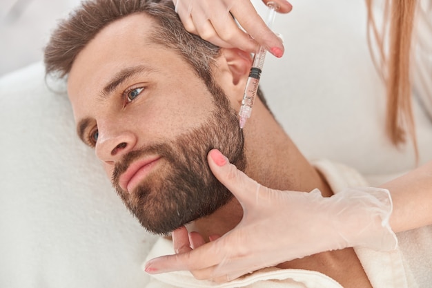 Photo close up makes mesotherapy injections to beard man. treatment of male by a beautician for hair growth.